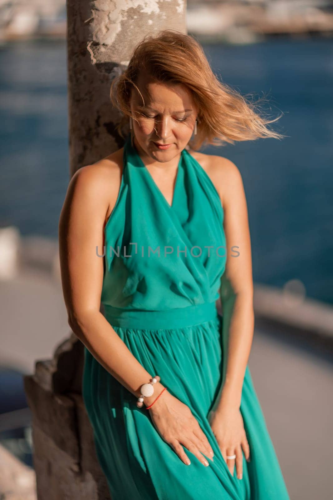 Happy blonde in a long mint dress posing against the backdrop of the sea in an old building with columns. Girl in nature against the blue sky. by Matiunina