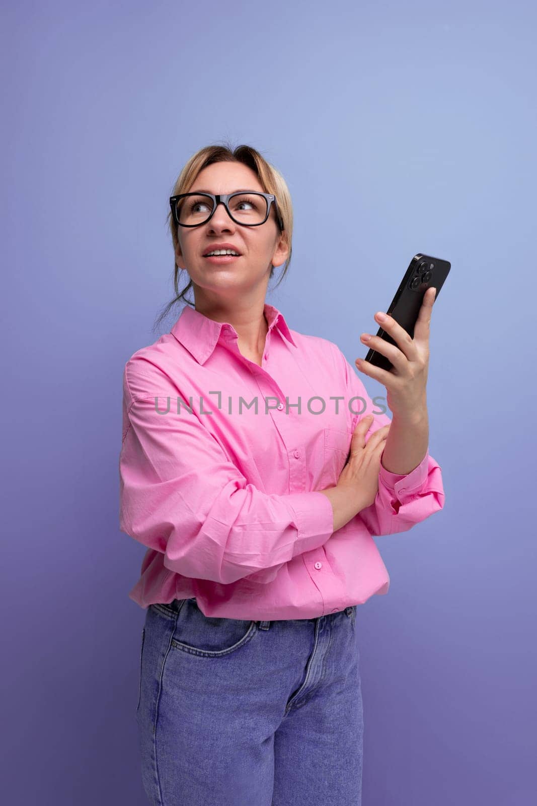 young confident blond woman with ponytail and glasses dressed in a fashionable pink shirt for the office solves work issues on the phone.