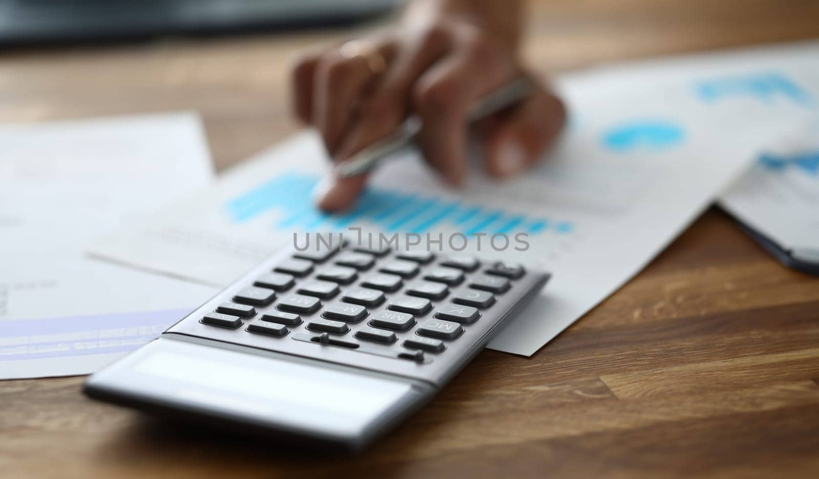 Close-up of calculator on wooden table. Accountant making annual financial statement. Worker preparing presentation with graphs, charts to meeting of directors. Business and finance concept