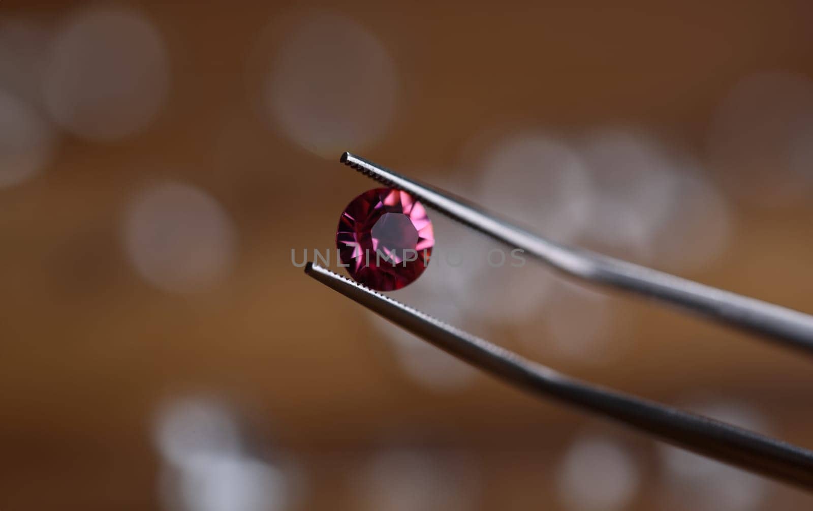 Close-up of tweezers holding gemstone. Professional jeweler using special equipment. Jeweller checking precious stone for identity. Jewelry production concept