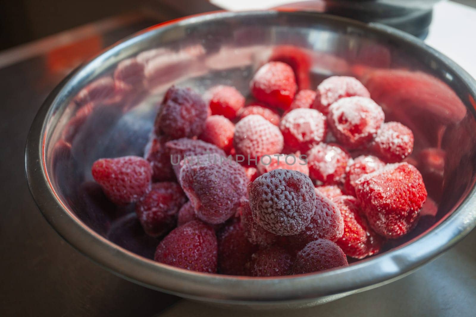 Close-up of frozen strawberries in an aluminum bowl on a kitchen counter.