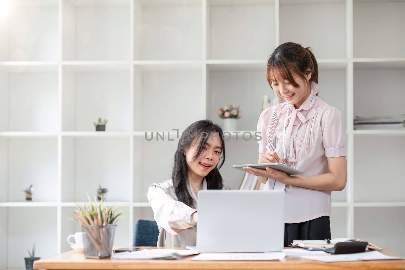 Two Young Asian businesswoman discuss with new startup project Idea presentation, analyze statistics and investment market at office by wichayada