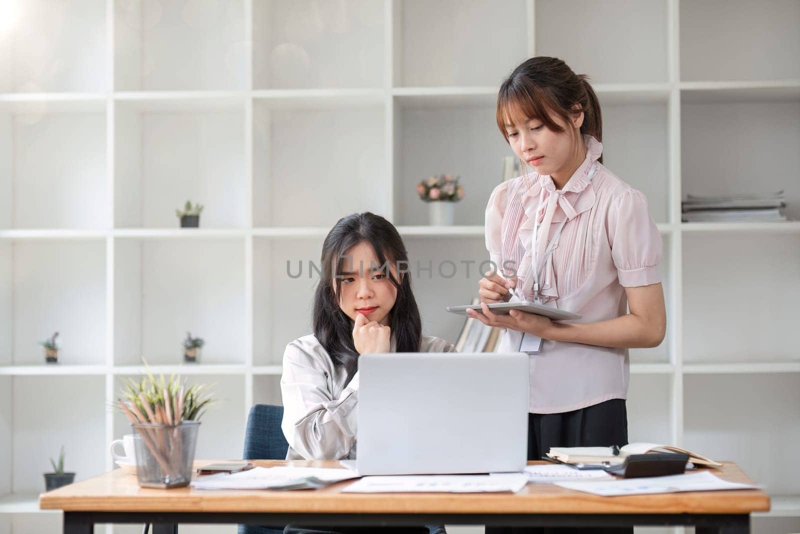 Two businesswomen colleagues working together look at laptop screen, talking about project, thinking, search solution, discuss business meet in modern office. Teamwork, workflow using tech.