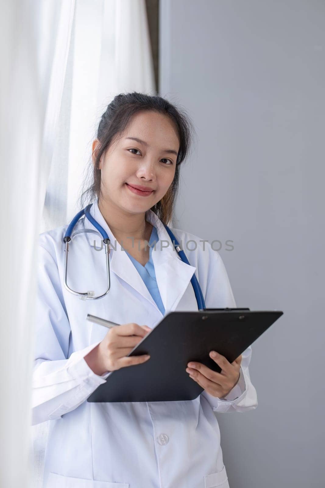 Portrait of female doctor wearing white coat with stethoscope holding clipboard and looking confidently to camera.