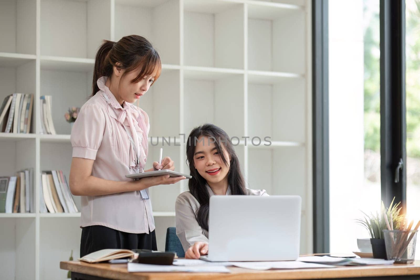 Two Young Asian businesswoman discuss with new startup project Idea presentation, analyze statistics and investment market at office by wichayada