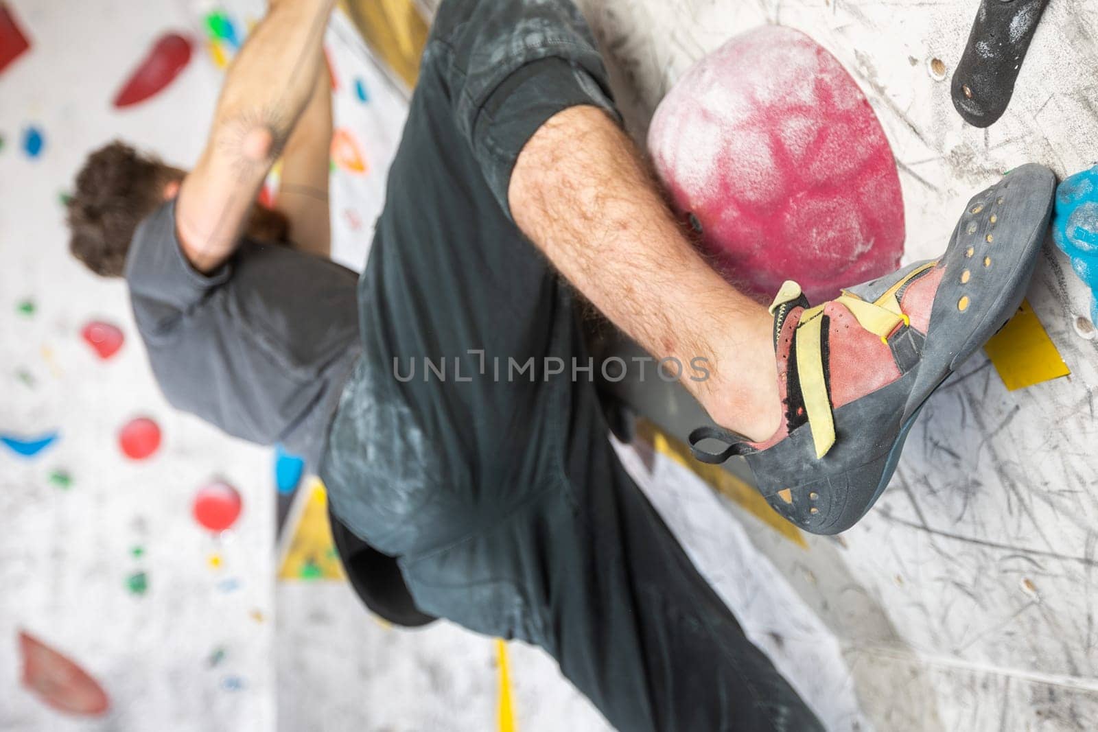 Young climber climbing on a boulder wall indoor, rear view, concept of extreme sports and bouldering