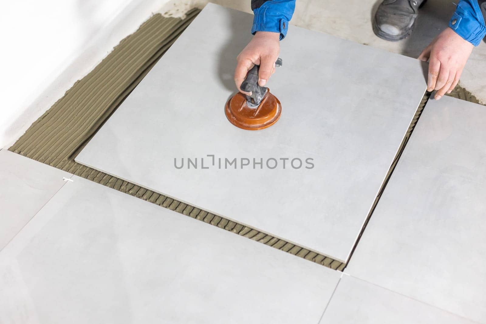 Tiler worker placing or tiling gray ceramic tile in position over adhesive glue with lash tile leveling system, renovation or recontruction, concept of building
