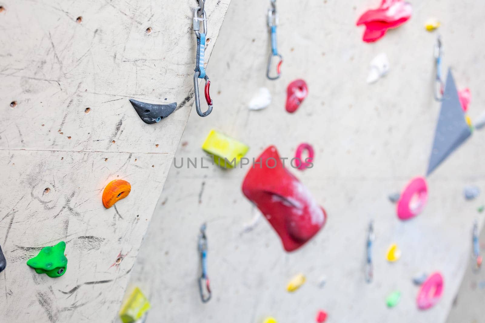 Close up of indoor climbing wall with carbines and colored grips fix it on a wall, concept of climbing