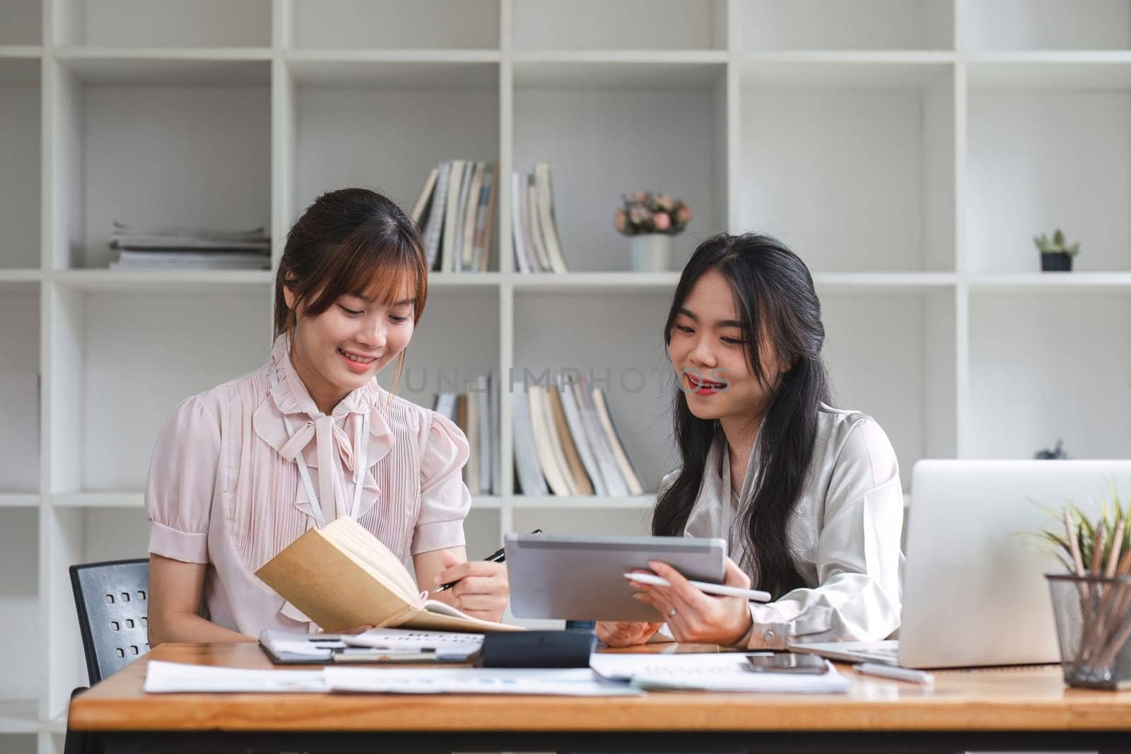 Two Young Asian businesswoman discuss with new startup project Idea presentation, analyze statistics and investment market at office by wichayada