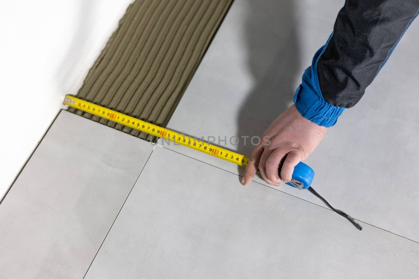 Tiler worker placing or tiling gray ceramic tile in the position over adhesive glue with lash tile leveling system, renovation or recontruction, concept of building by Kadula