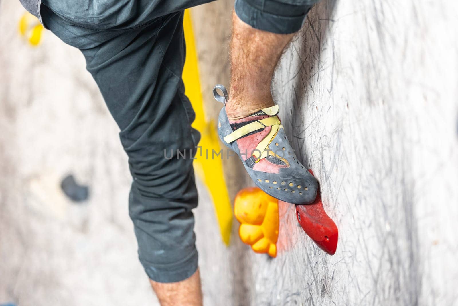 Close up view of young man or climber feet in climbing shoes on an artificial indoor wall at climbing center, sport activity concept
