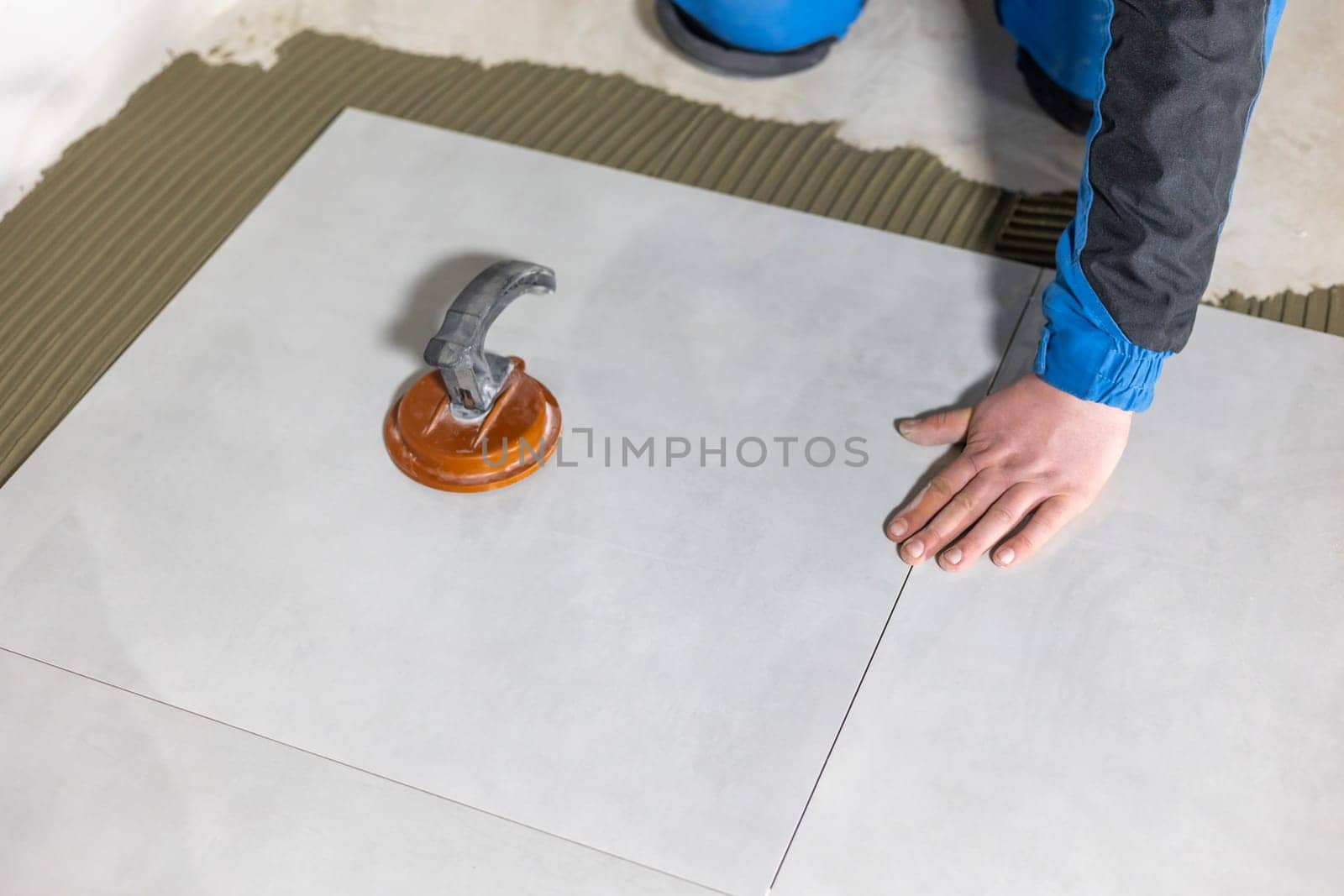 Tiler worker placing or tiling gray ceramic tile in a position over adhesive glue with lash tile leveling system, renovation or recontruction, concept of building