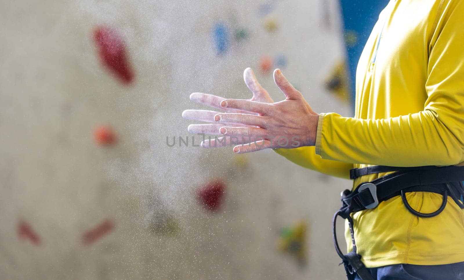 Athletic young man using magnesium for a dry hands, dust flies from talcum powder, white chalk powder, indoor wall climbing concept