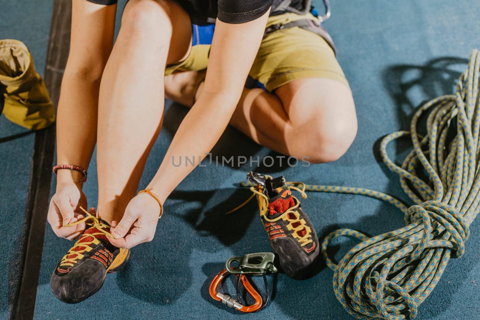 Young woman climber prepare before to climbing on a boulder wall indoor with equipment, shoe, rope, carabiner, concept of extreme sports and bouldering