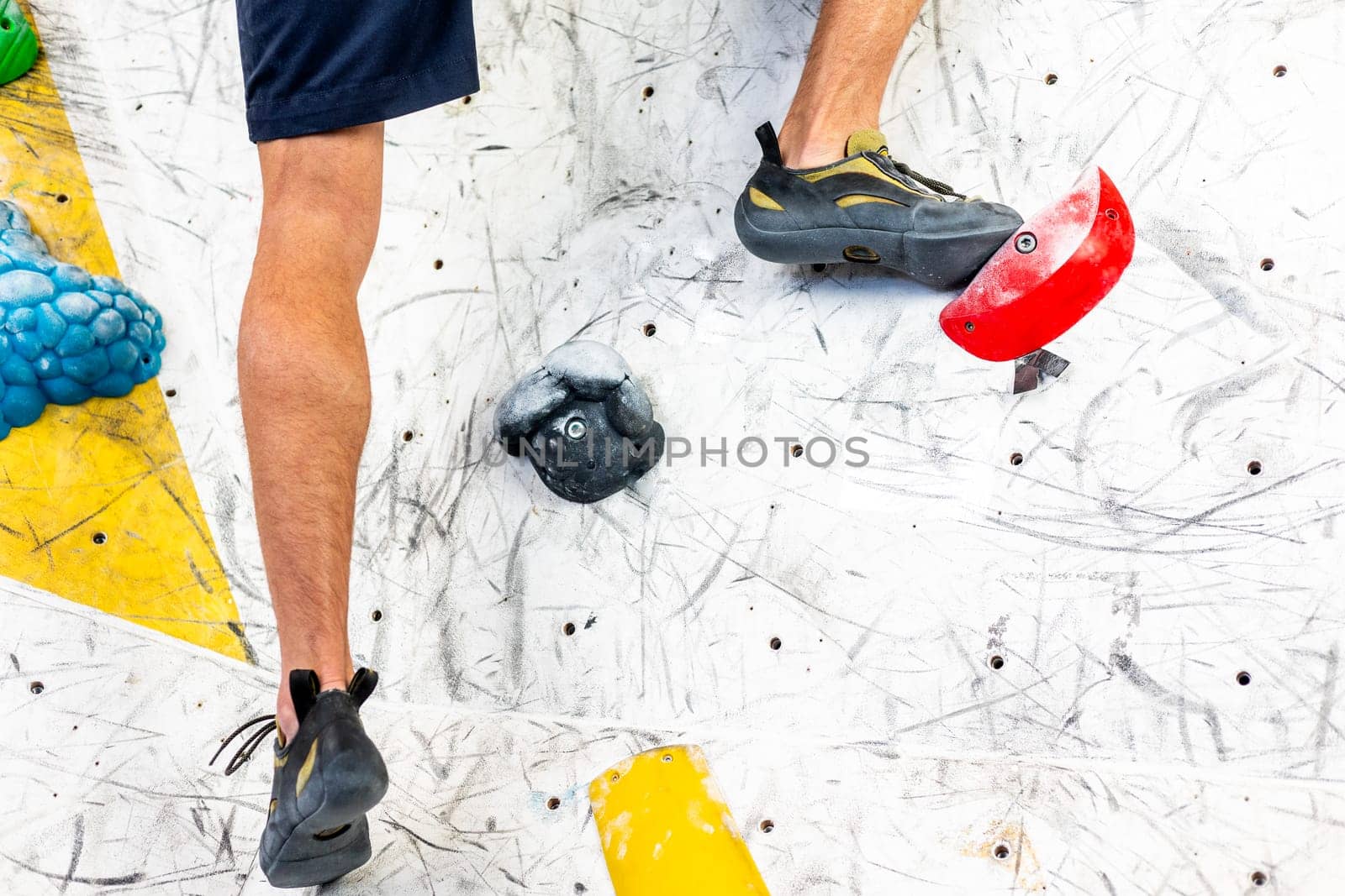Close up view of young man or climber feet in climbing shoes on artificial indoor wall at the climbing center, sport activity concept