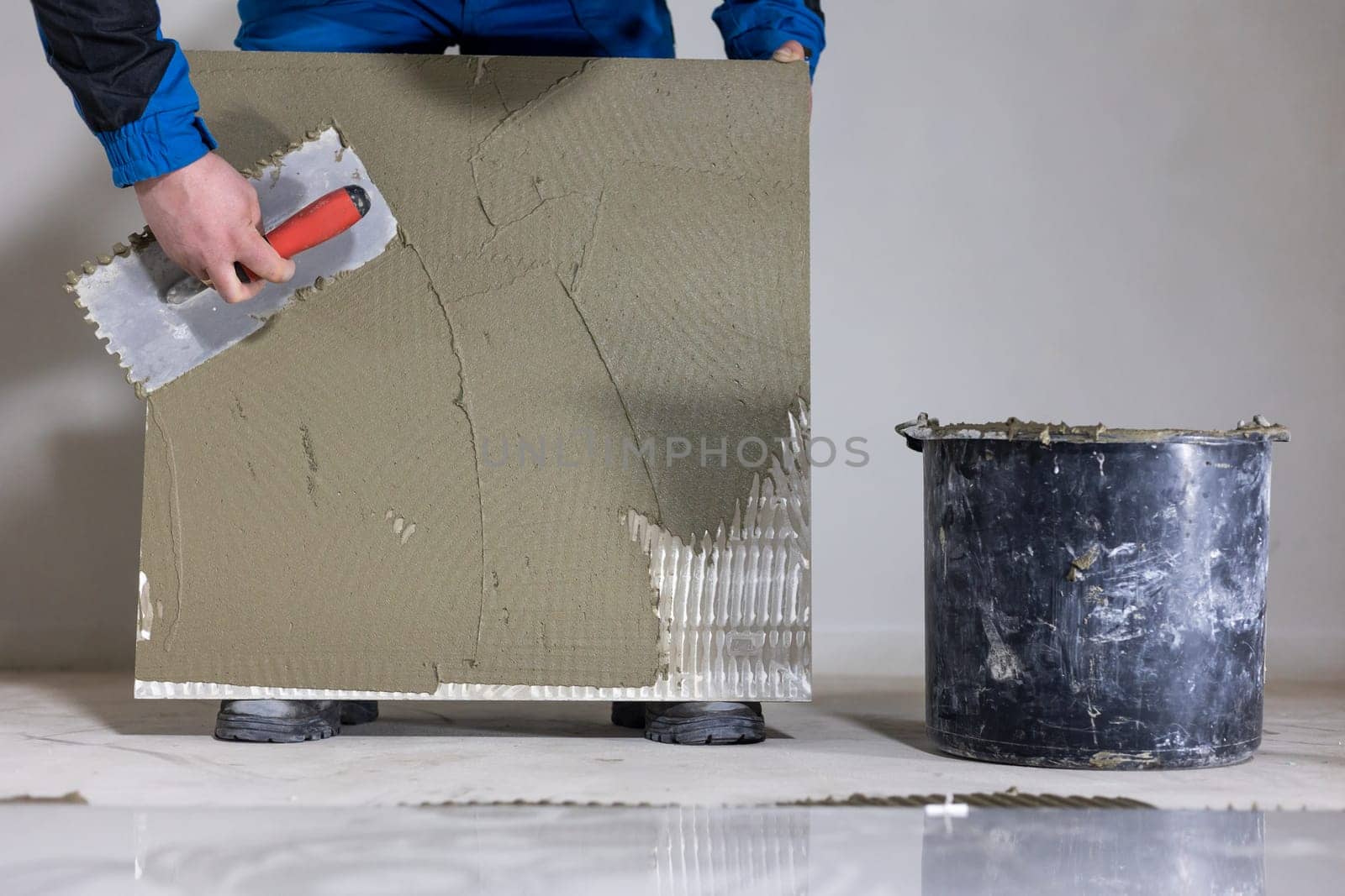 Tiler worker placing or tiling gray ceramic tile in position over adhesive glue with lash tile leveling system, renovation or recontruction, concept of building