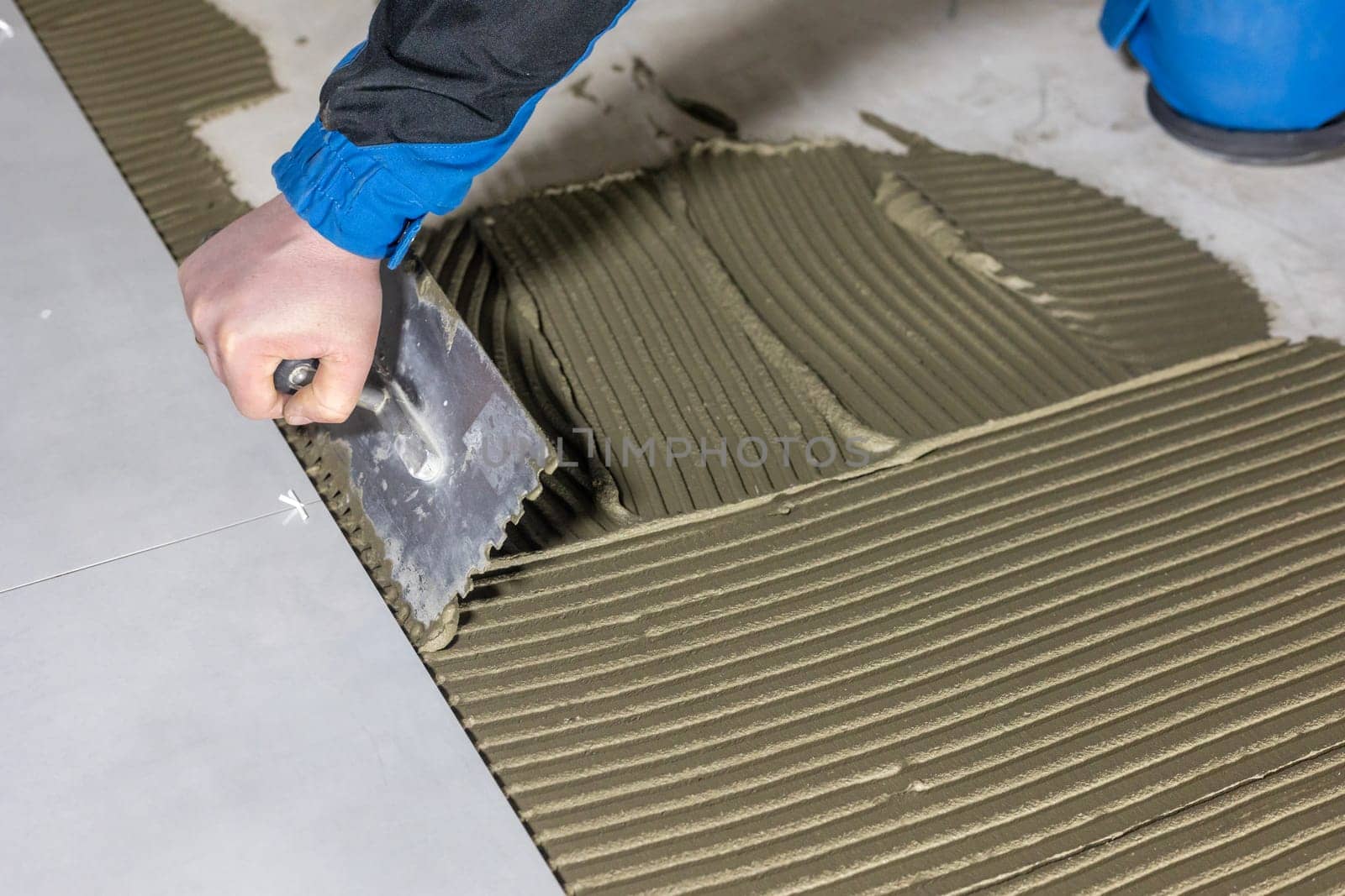 Tiler worker placing or tiling gray ceramic tile in position over adhesive glue with lash tile leveling system, renovation or recontruction, concept of building