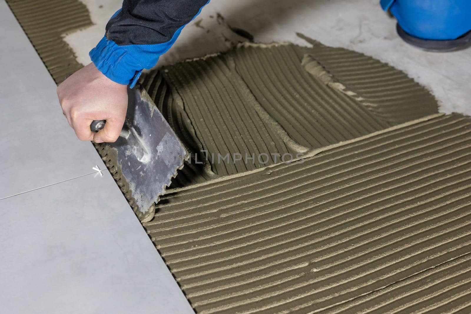 Tiler worker placing or tiling gray ceramic tile in position over adhesive glue with lash tile leveling system, renovation or recontruction, concept of building