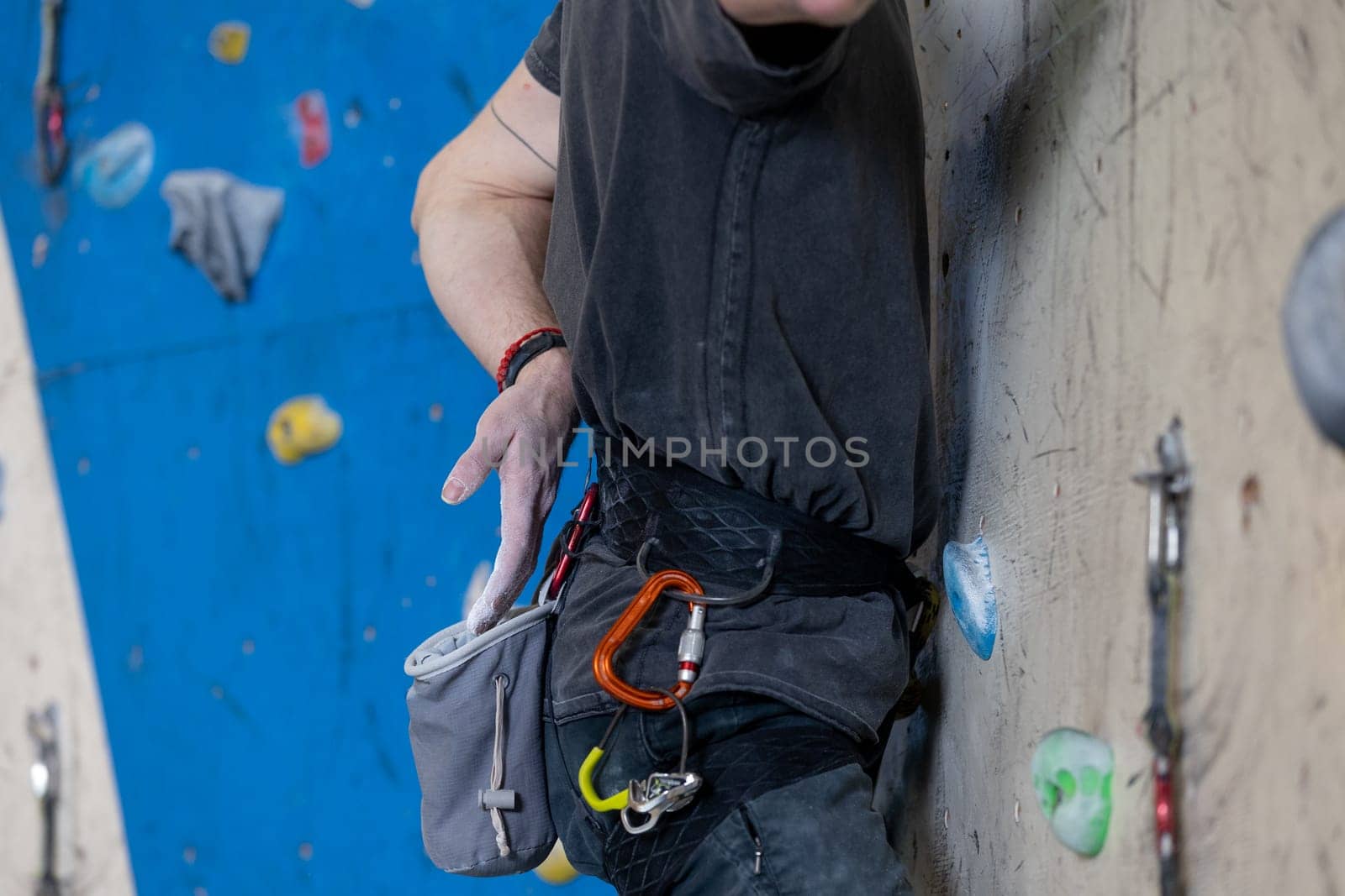 Young climber man coating his hands in powder chalk or magnesium and preparing to climb indoor, concept of extreme sports and bouldering by Kadula