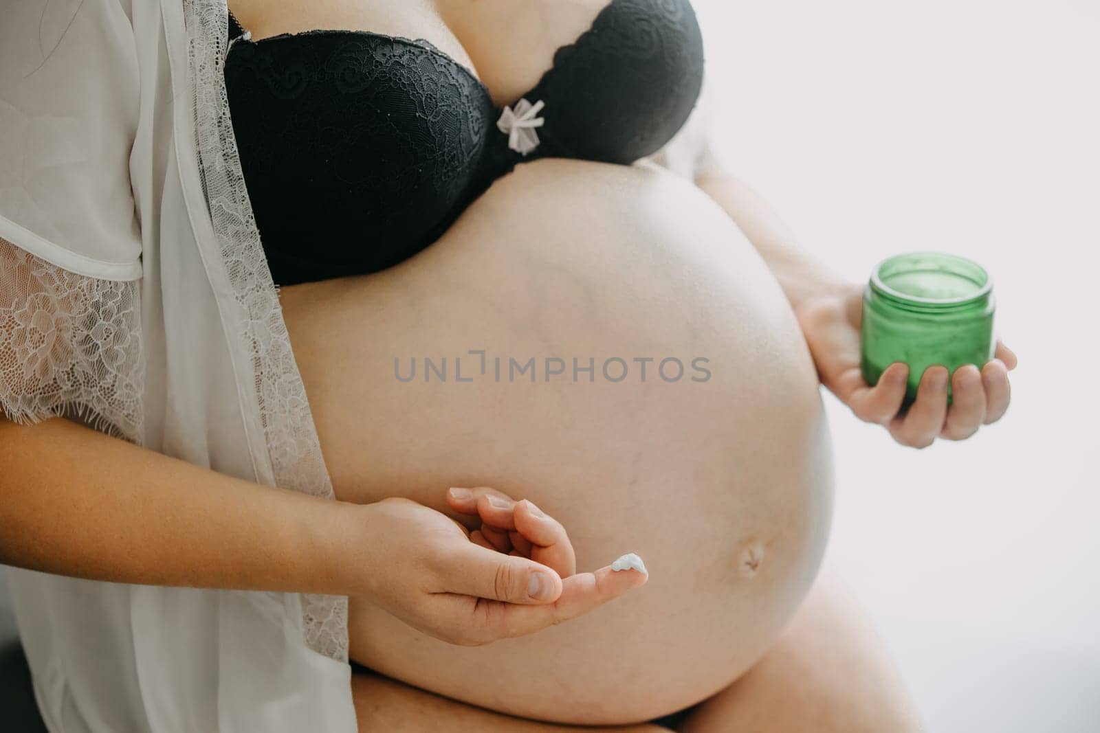 Young pregnant woman with the belly smearing cream against the stretch marks, pregnancy concept