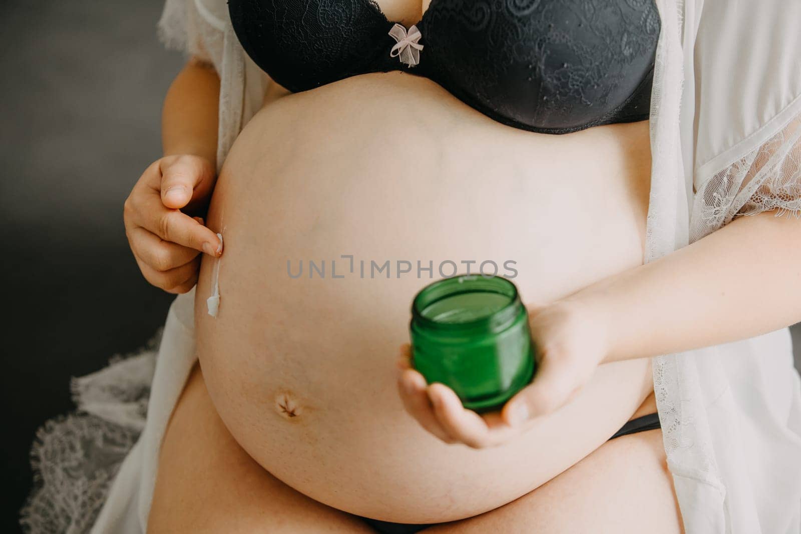 Young pregnant woman with the belly smearing cream against the stretch marks, pregnancy concept