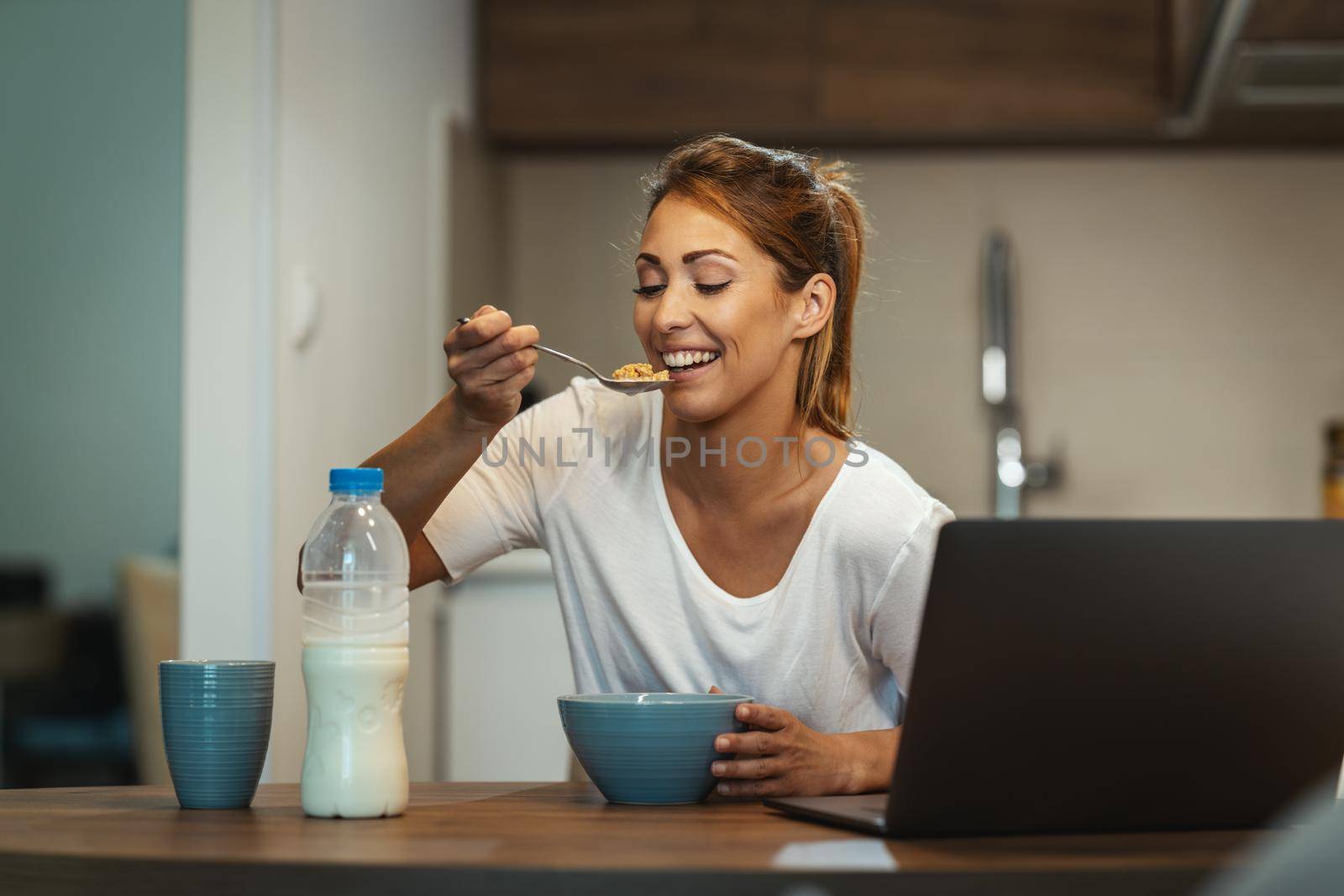 Beautiful young woman is eating her healthy breakfast in her kitchen.