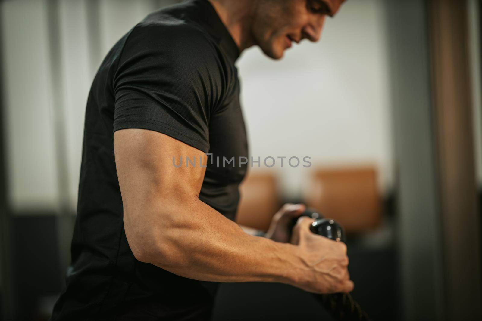 Muscular young man in sportswear focused on doing cable triceps pulldowns during a strength training workout at the gym.