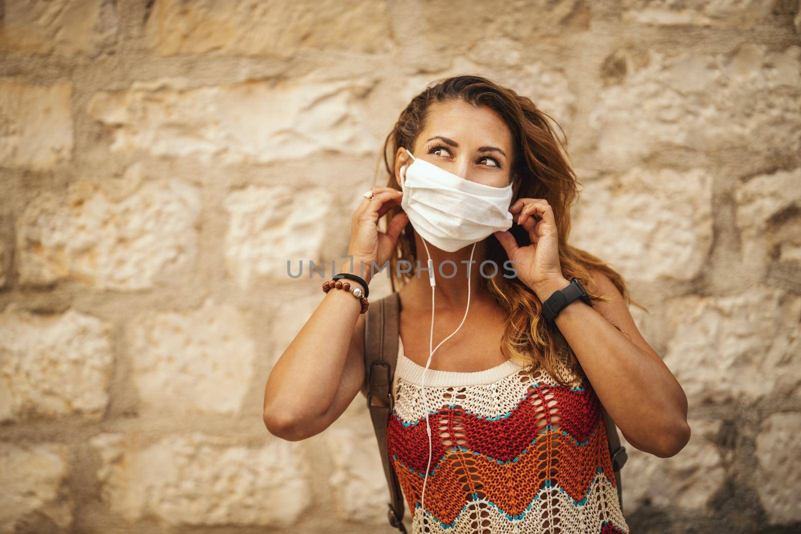 Shot of a happy young woman with protective mask spending time on vacation and having fun during exploring a Mediterranean city at corona pandemic. 