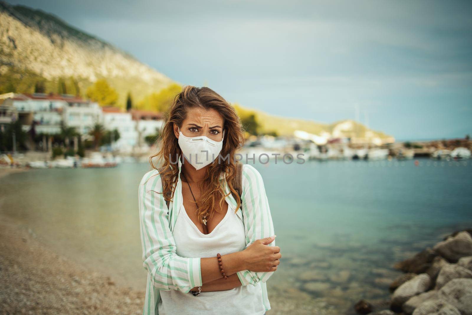 Pensive young woman with protective N95 mask feeling worried while spending time on the seaside during the COVID-19.