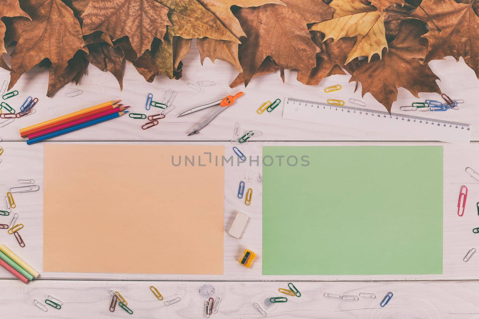 Empty colored papers and school supplies on wooden table with autumn leaves.Image is intentionally toned.