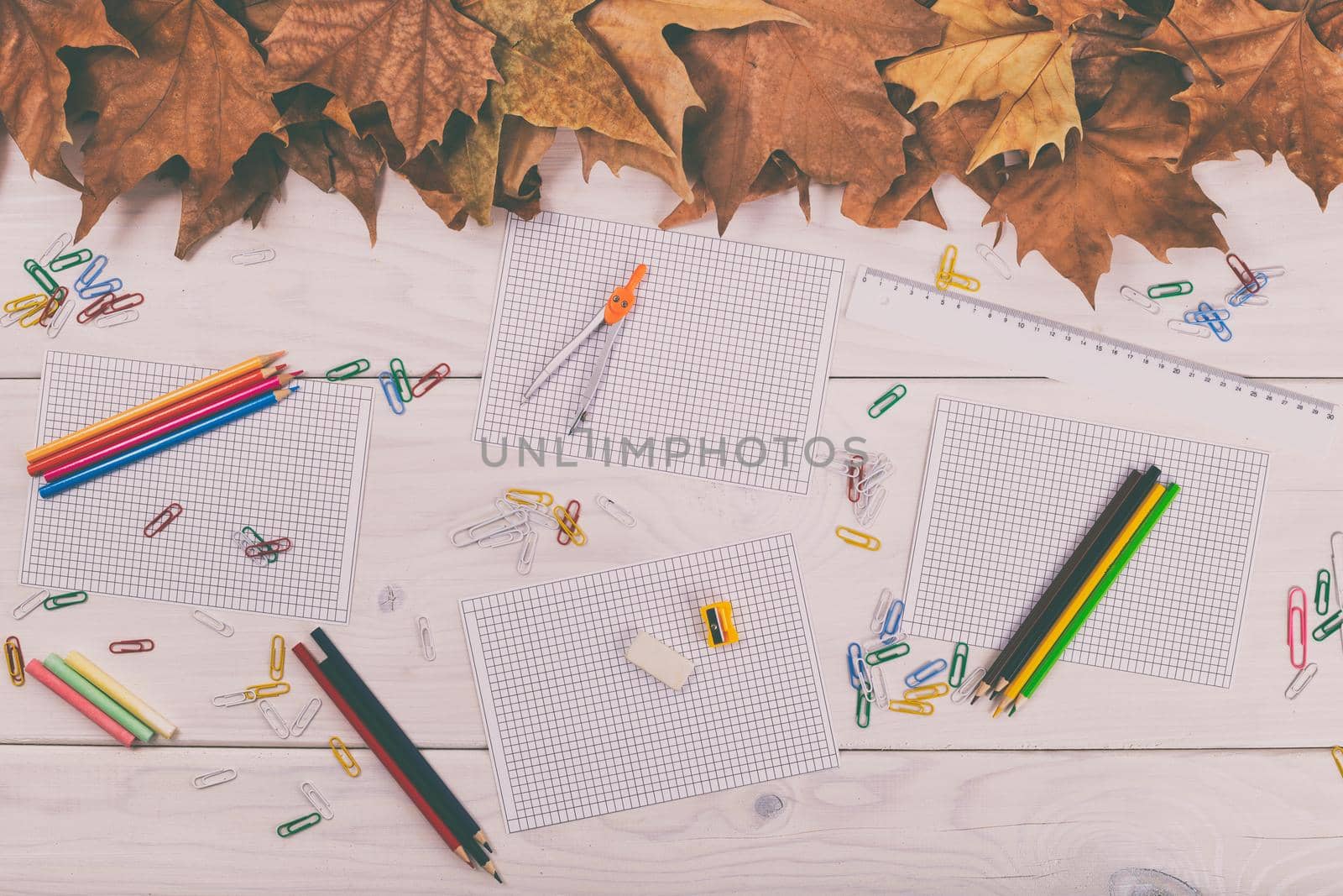 Empty papers and school supplies on wooden table with autumn leaves.Image is intentionally toned.