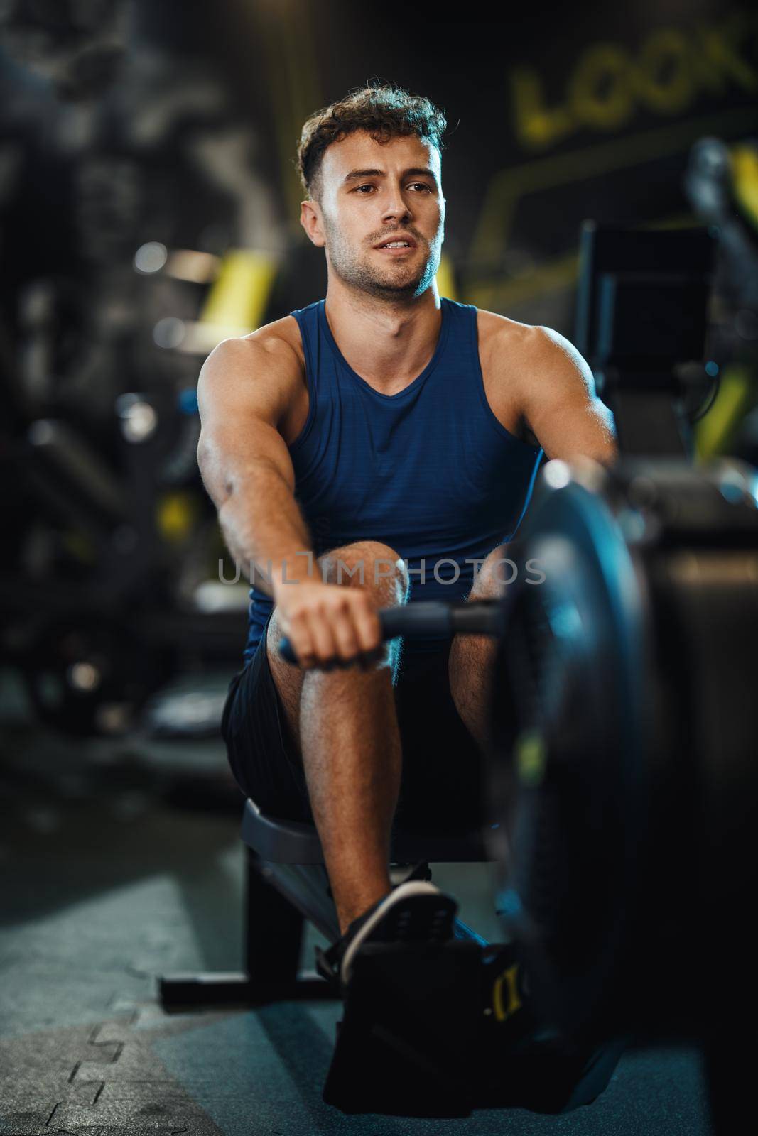 A young muscular man is pulling the row machine on crossfit training in the gym.