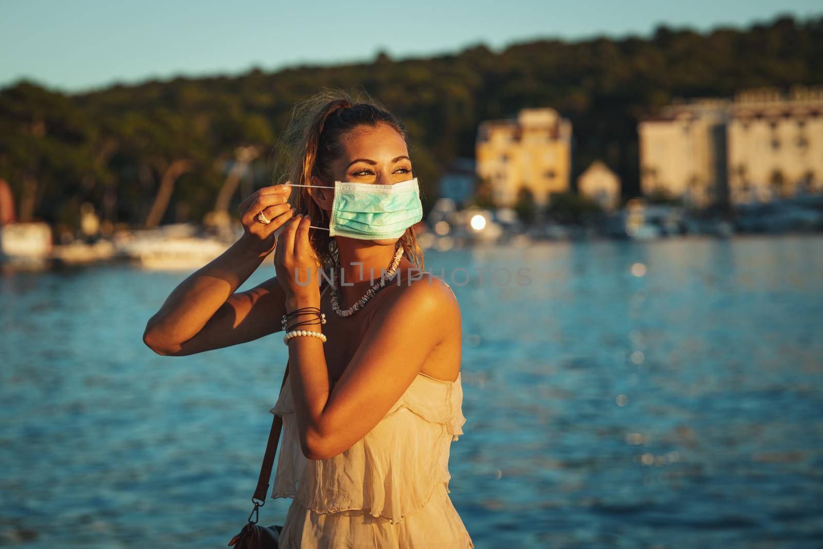 Shot of an attractive young woman wearing a surgical mask while enyoing herself during walk promenade by the sea.