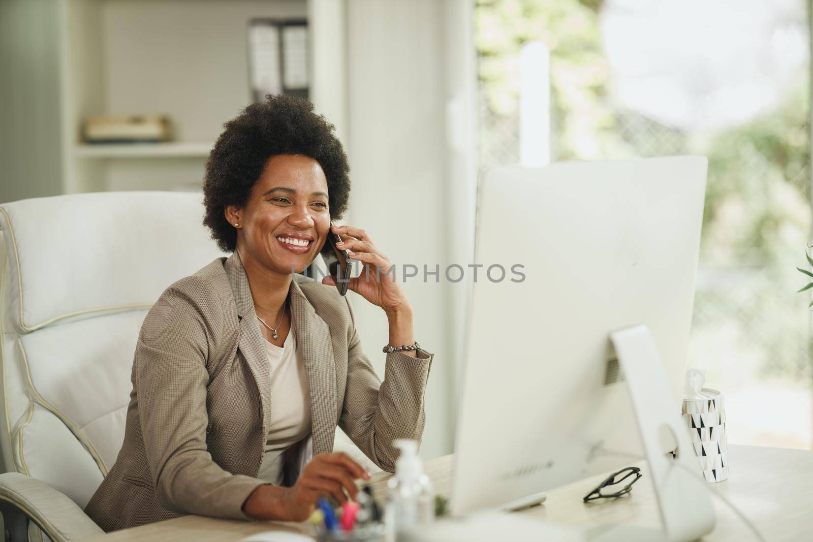 Shot of an African businesswoman talking on smartphone while working at desk in her home office during corona virus pandemic.