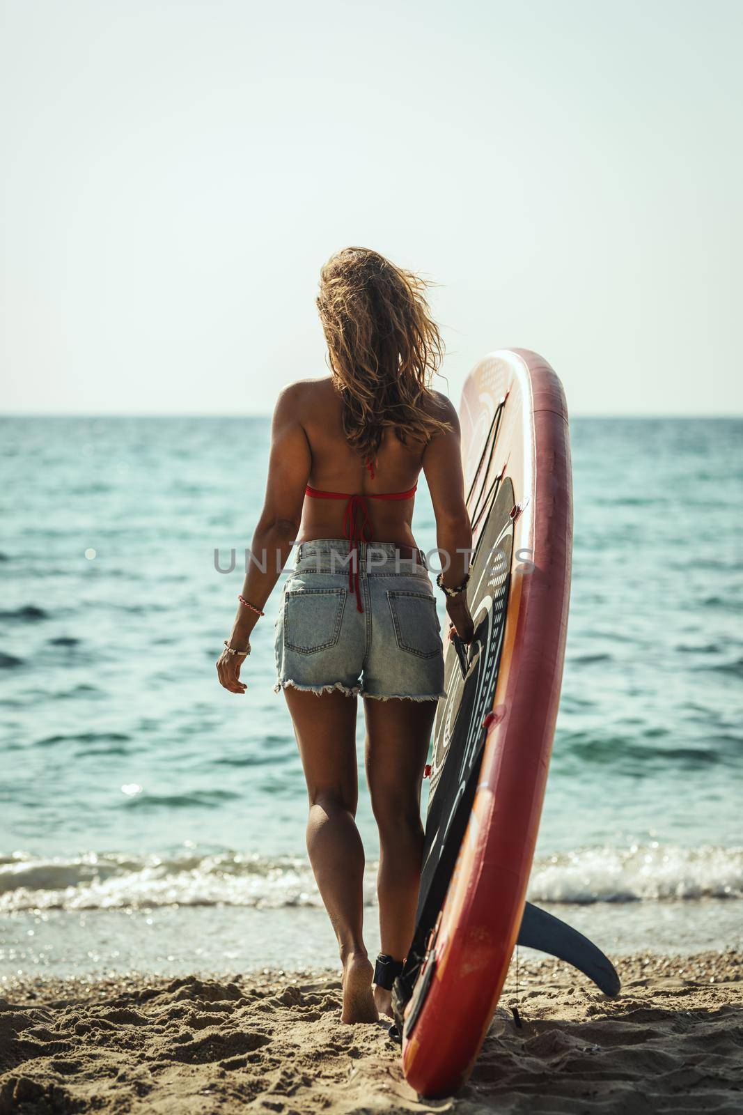 A young woman on a sea beach with a surfboard is ready for the waves.