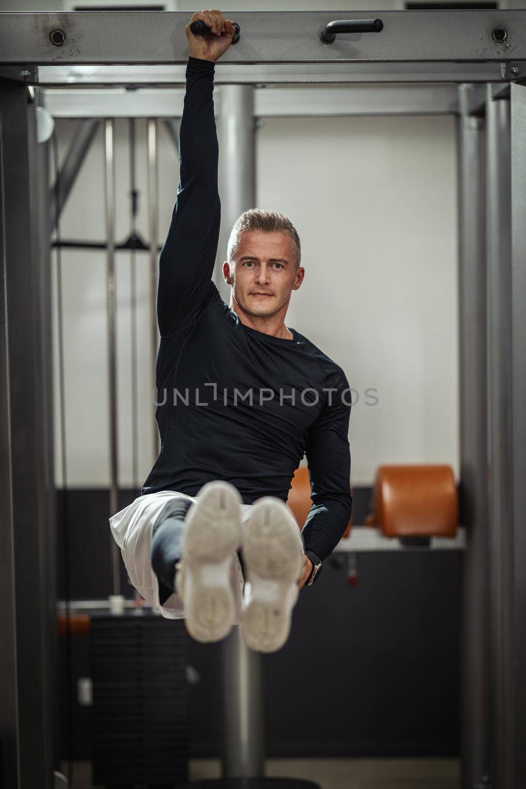 Muscular young man in sportswear focused on doing sit-up exercises during a strength training workout at the gym.