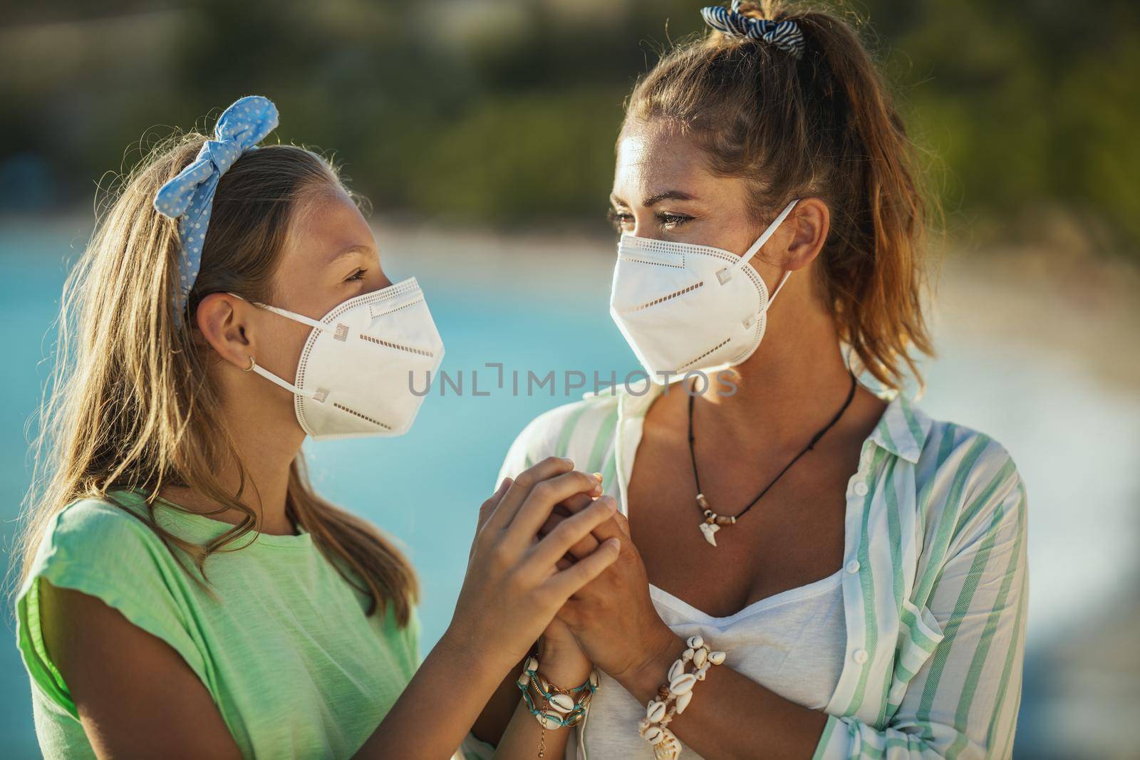 Shot of a smiling sisters with protective N95 mask spending time on the beach at corona pandemic. They are having self-isolation in nature.