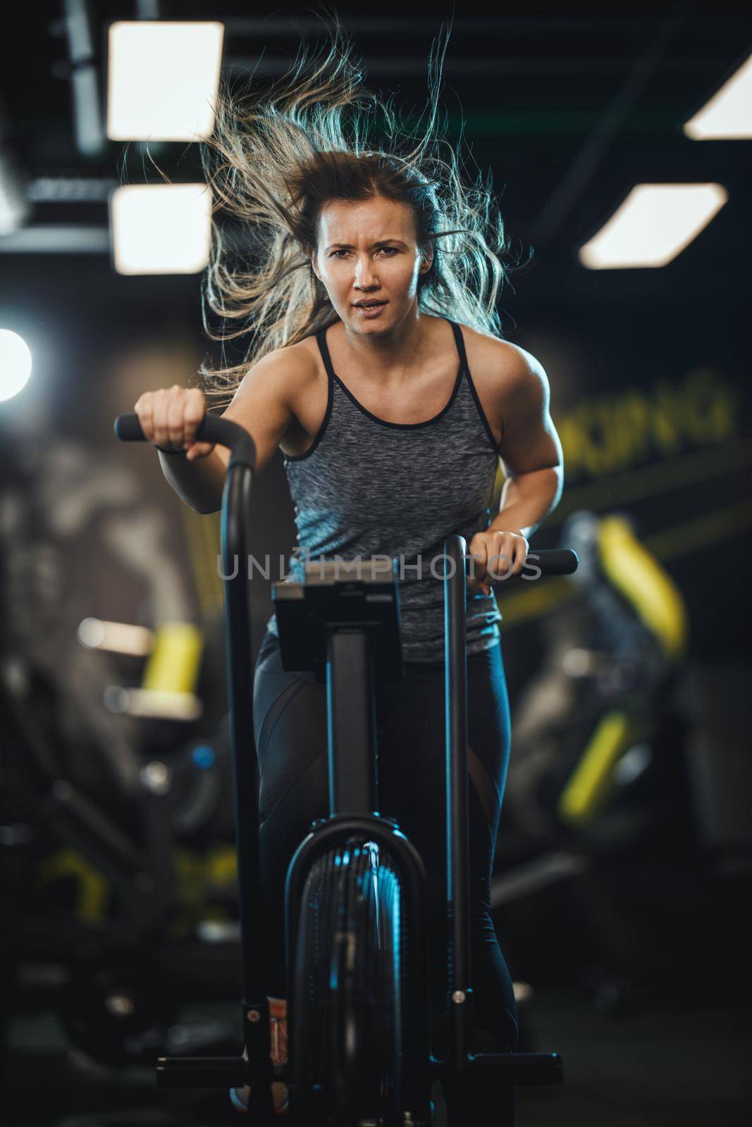 A young muscular woman is doing hard cal bike crossfit training in the gym.