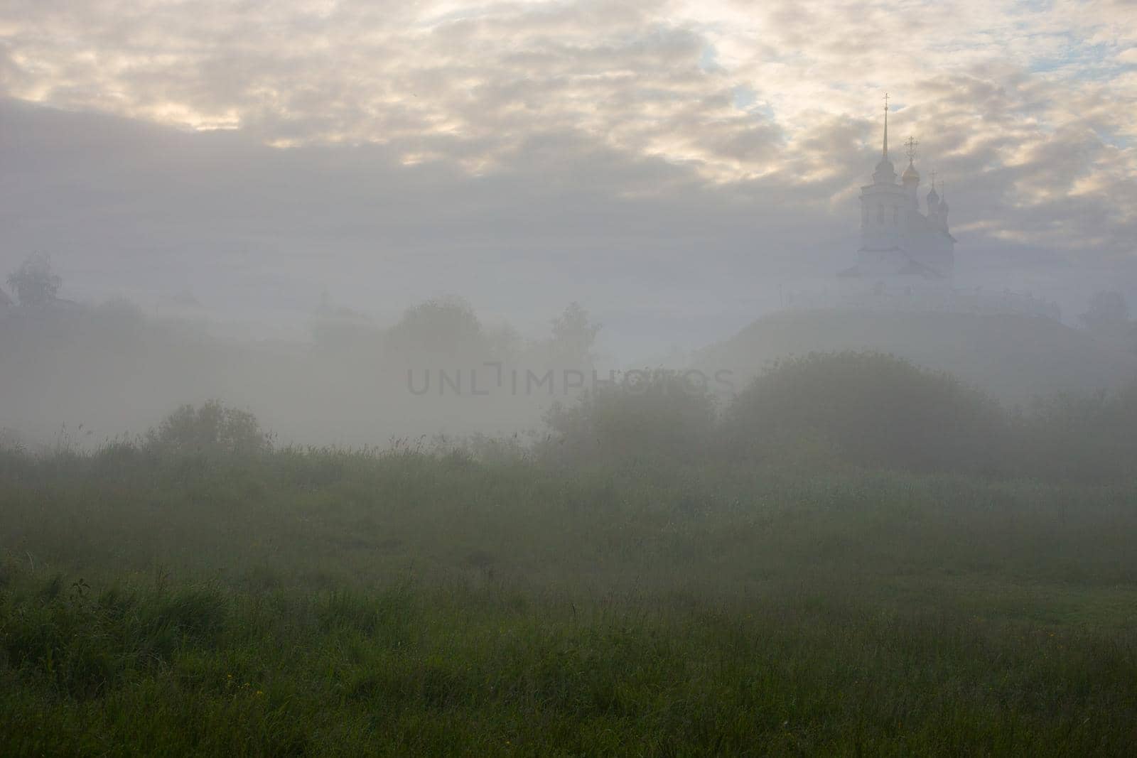 foggy summer morning landscape with the church on the hill in the background.