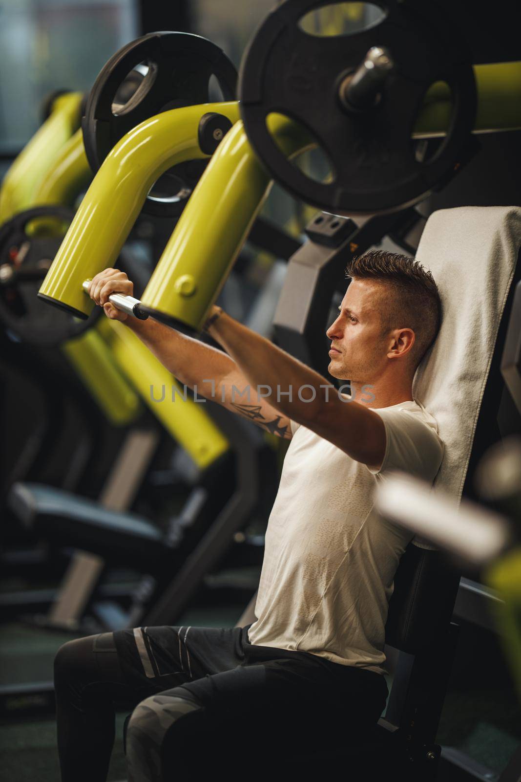Shot of a muscular guy in sportswear working out at the cross training gym. He is pumping up chest muscule with heavy weight.