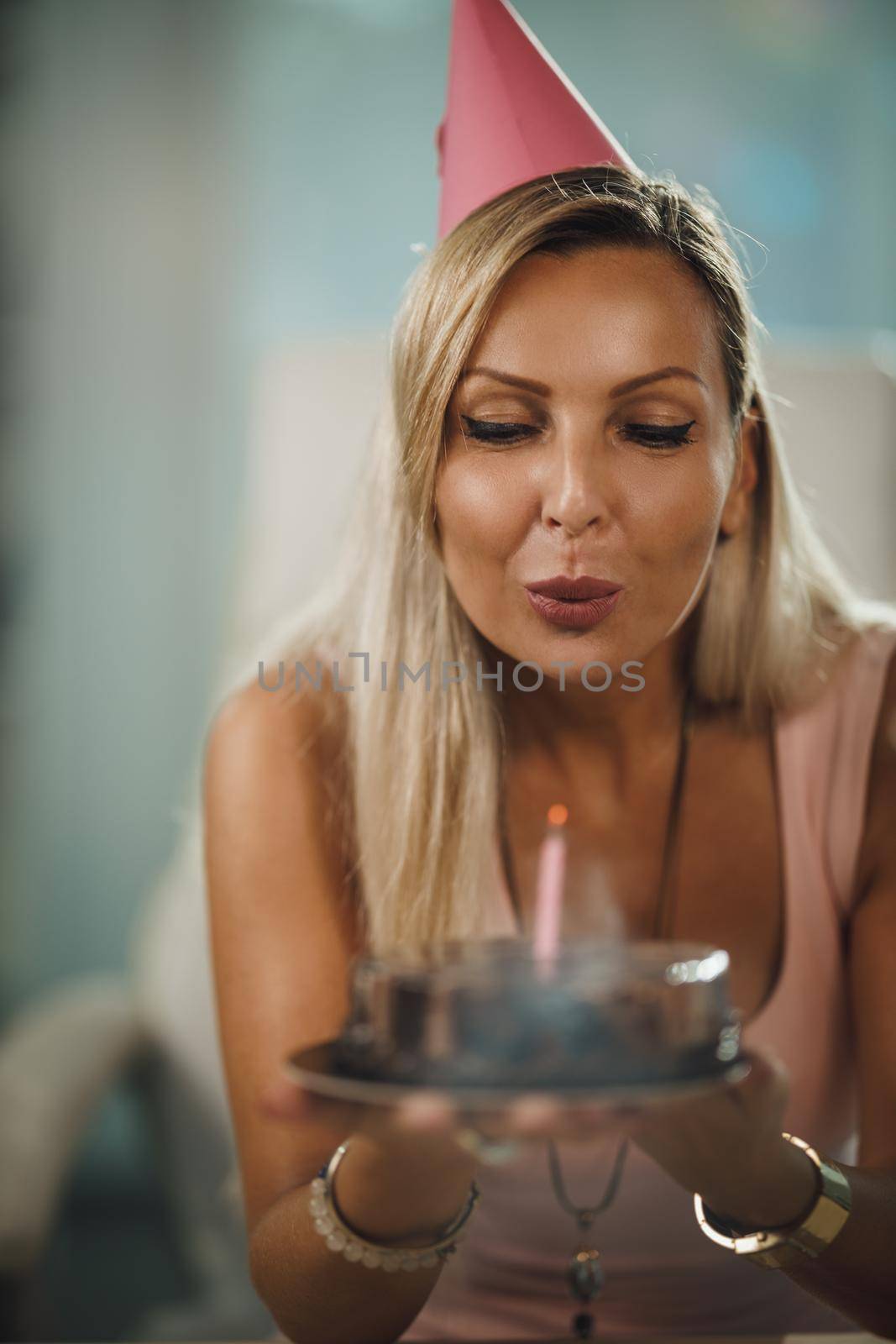 Alone attractive woman have birthday celebration at home during pandemic isolation and have video call with friends. She holding birthday cake with lighted candles.