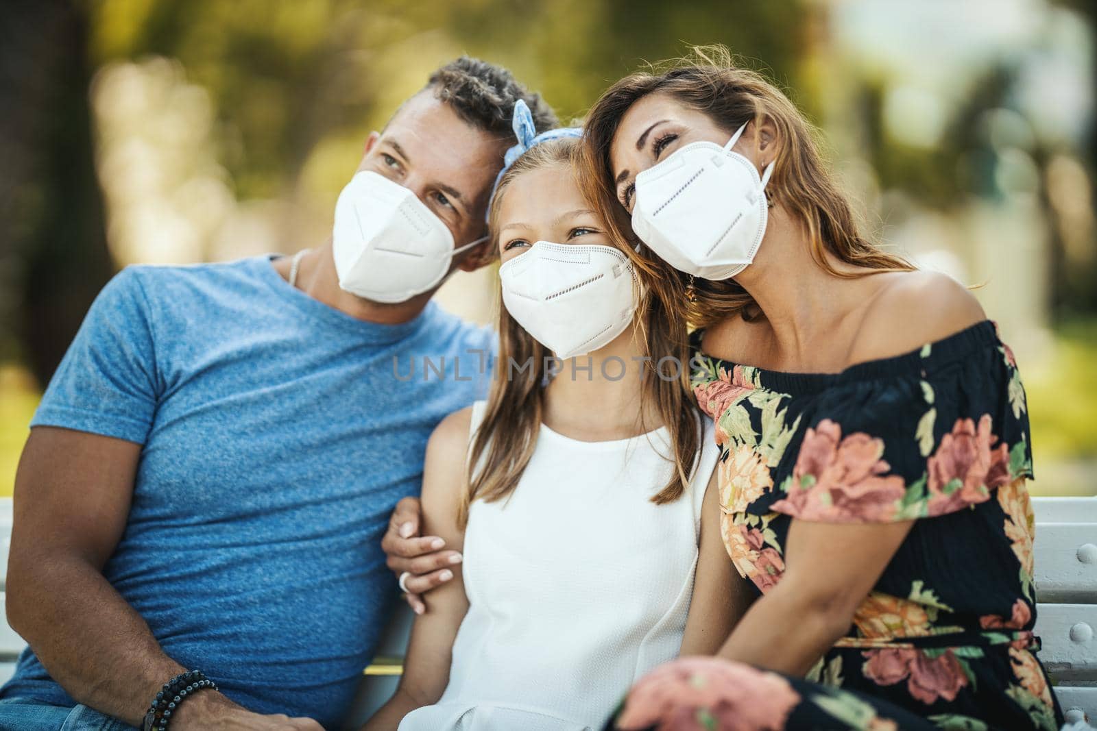 Self-isolation in nature. Young happy family with protective N95 mask having fun during spending time in the park at corona pandemic.