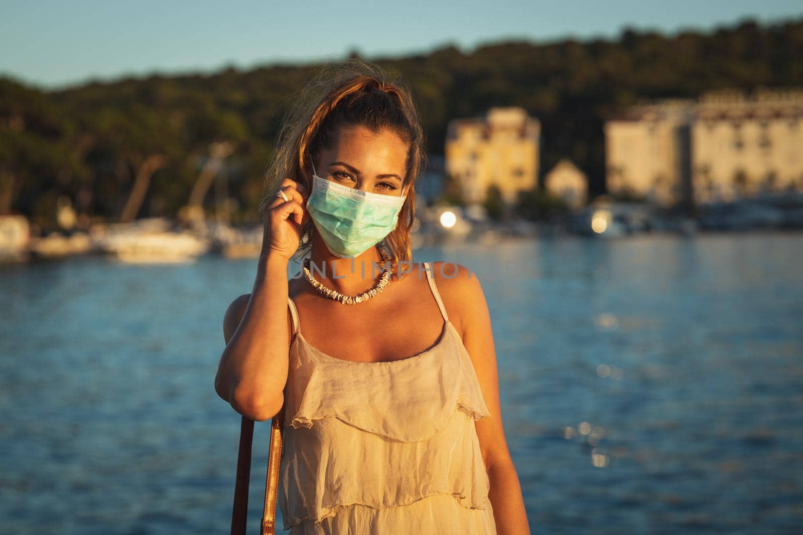 Portrait of an attractive young woman wearing a surgical mask while enyoing herself during walk promenade by the sea.