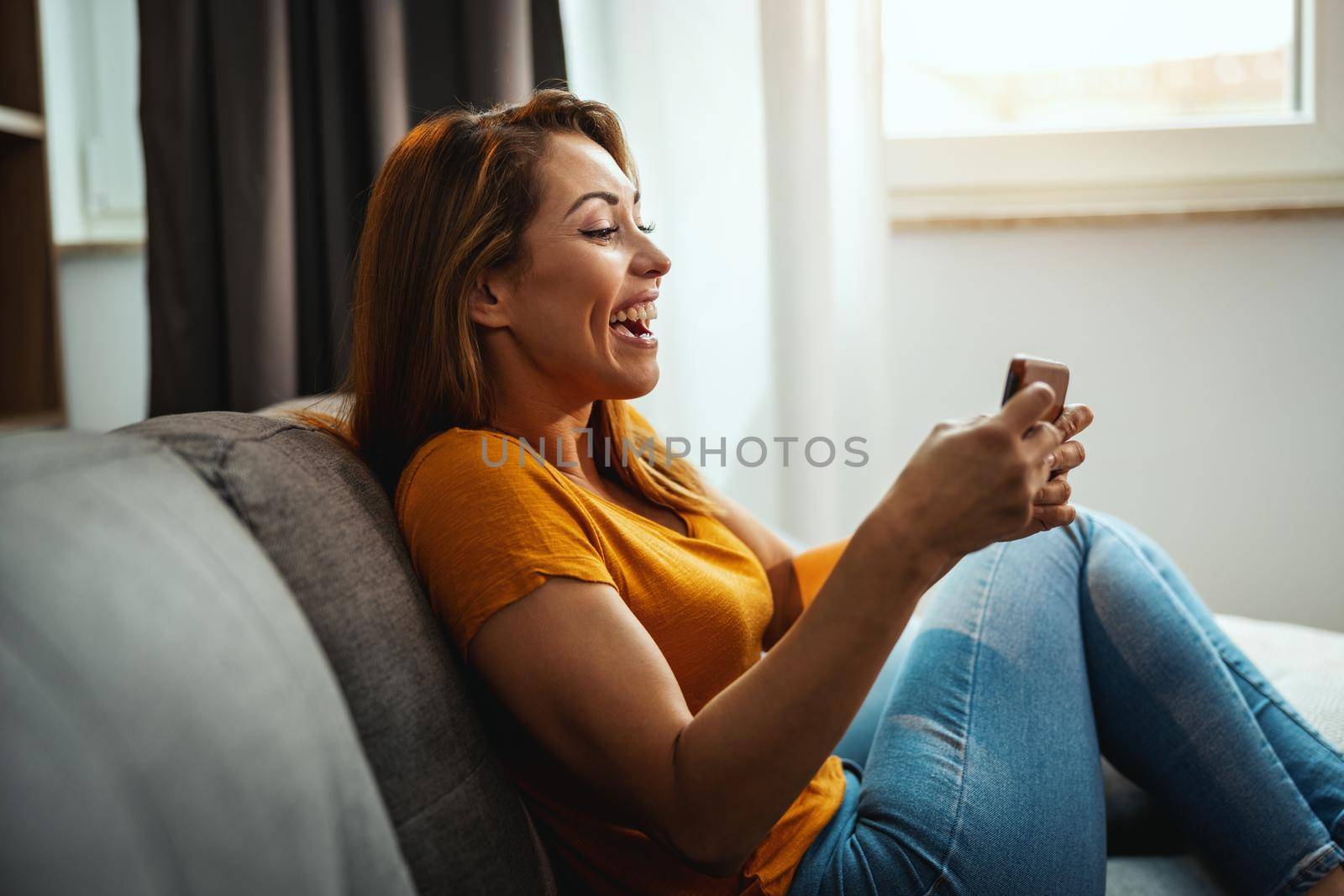 Attractive young woman sitting on the sofa and using smartphone to playing video game at home.