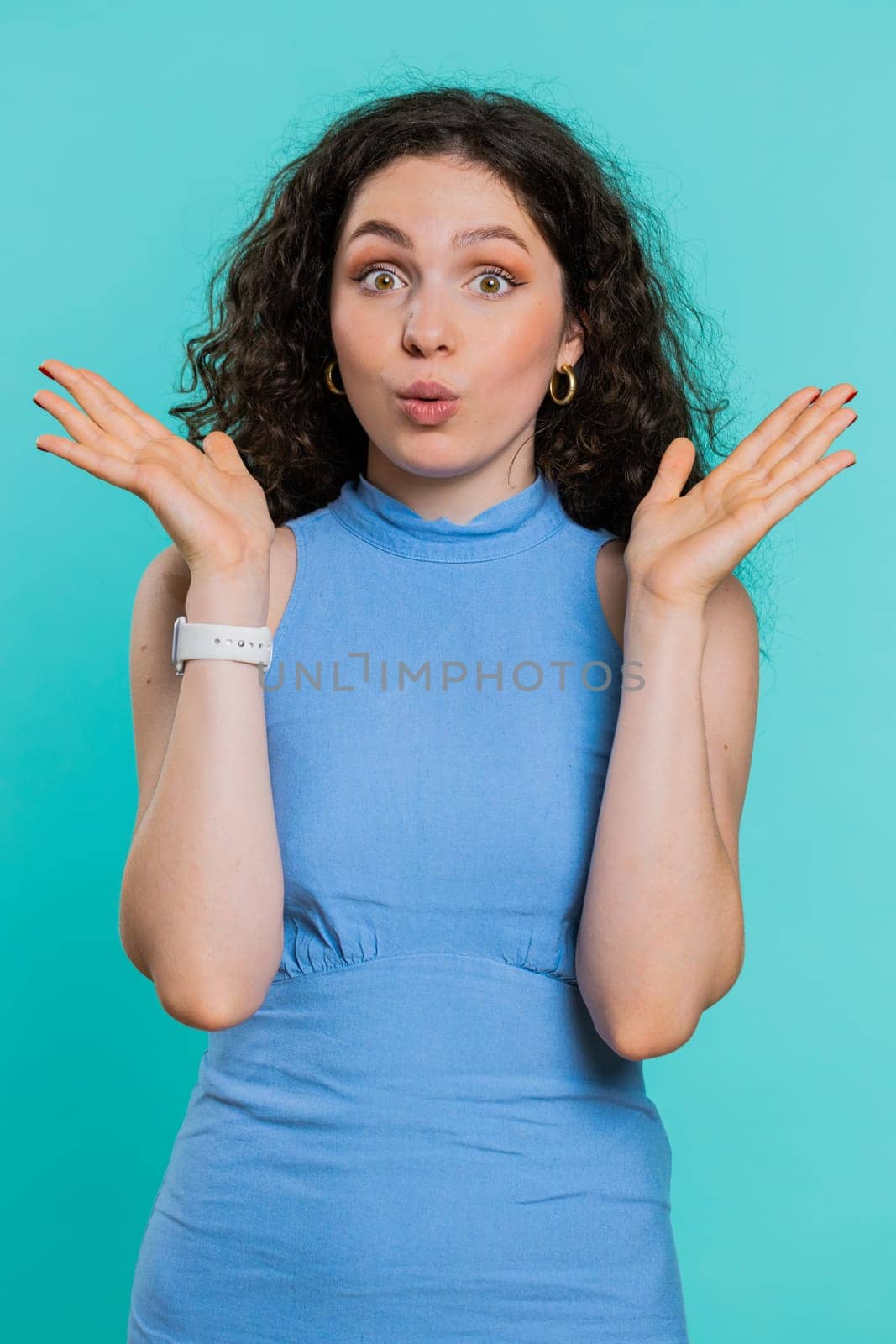 Oh my God, Wow. Excited amazed winner woman raising hands in surprise looking at camera with big eyes, shocked by sudden victory. Sincere attractive girl isolated on blue studio background. Vertical