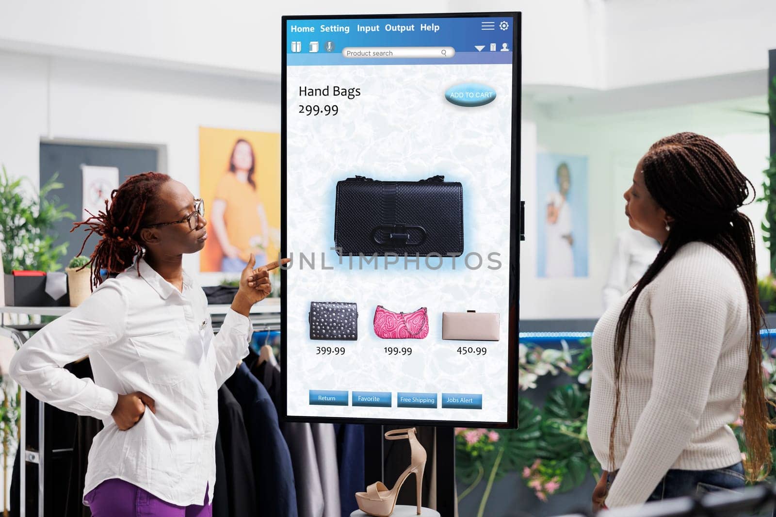 Store assistant showing items to woman in front of self ordering service kiosk, selecting fashion collection clothes to buy in clothing boutique. Customer talking to employee about products.