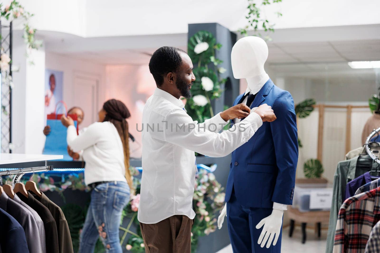 Man dressing mannequing in formal outfit in clothing store by DCStudio