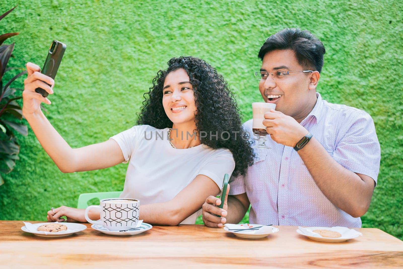 Couple of friends sitting enjoying a coffee and taking a selfie. Two happy friends having a coffee and taking a selfie by isaiphoto