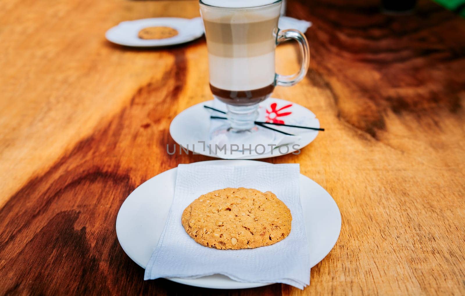 Close up of biscuit with cappuccino on wooden table. Delicious glass of hot cappuccino with cookie on wooden background by isaiphoto