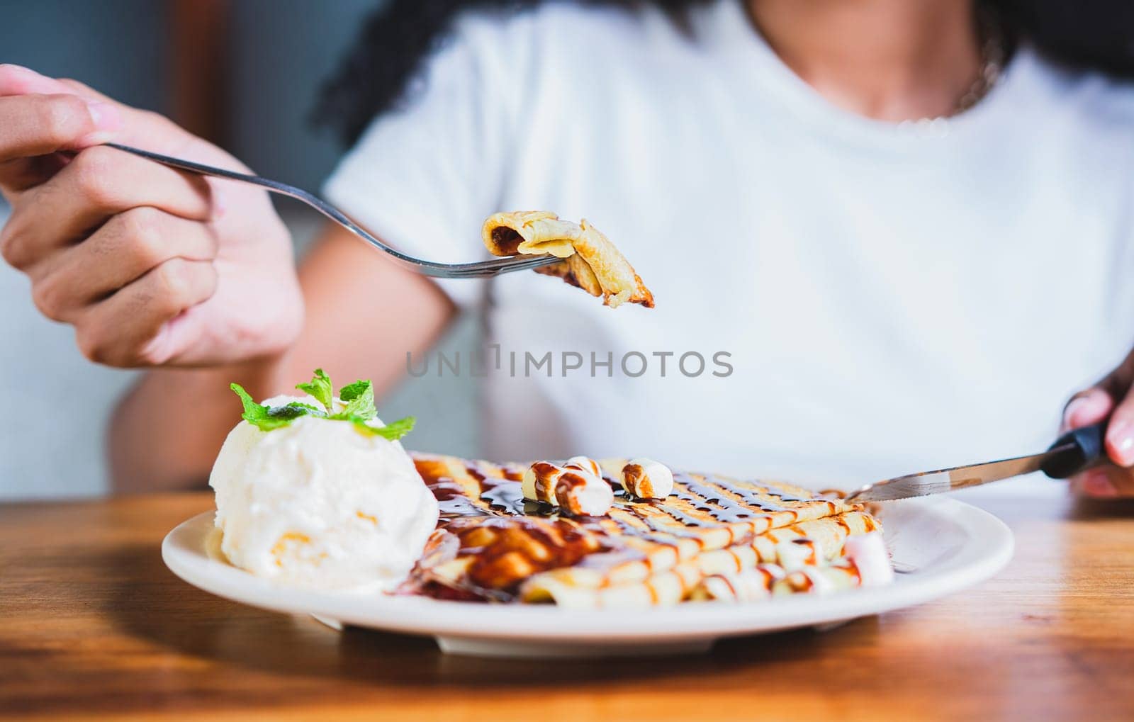 Close up of woman eating chocolate crepe and ice cream with fork. Hands of person with fork cutting chocolate crepe and ice cream by isaiphoto